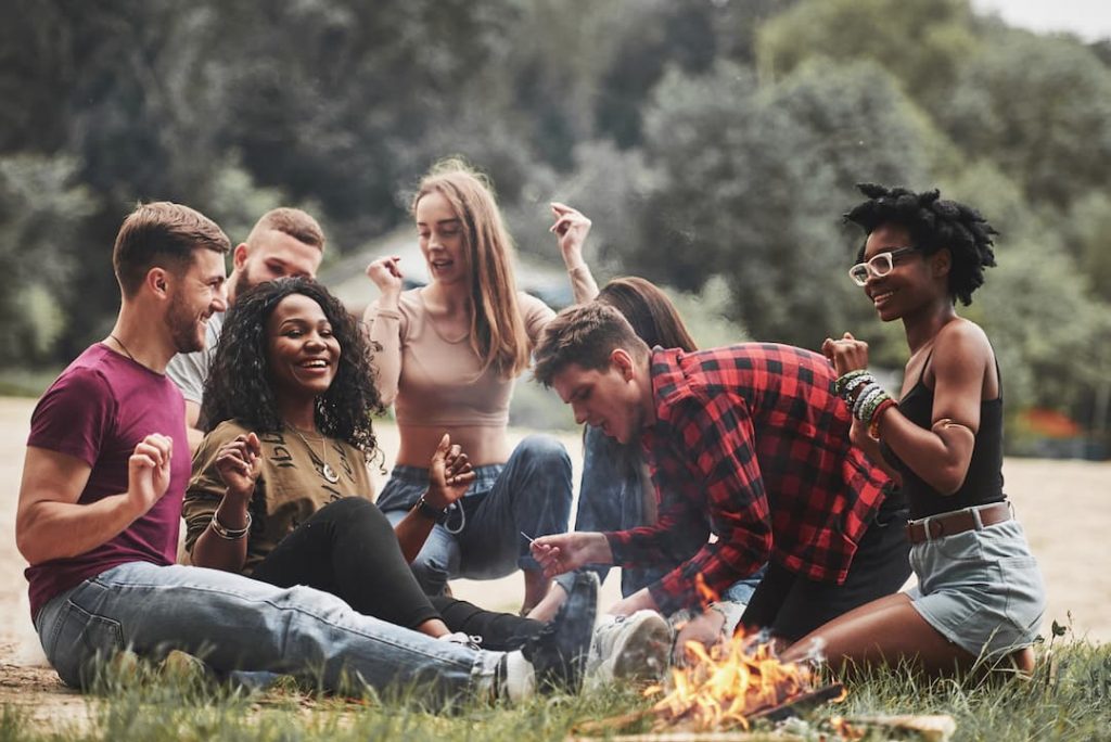 Group of friends laughing around a camp fire | Featured image for best board games for camping blog.