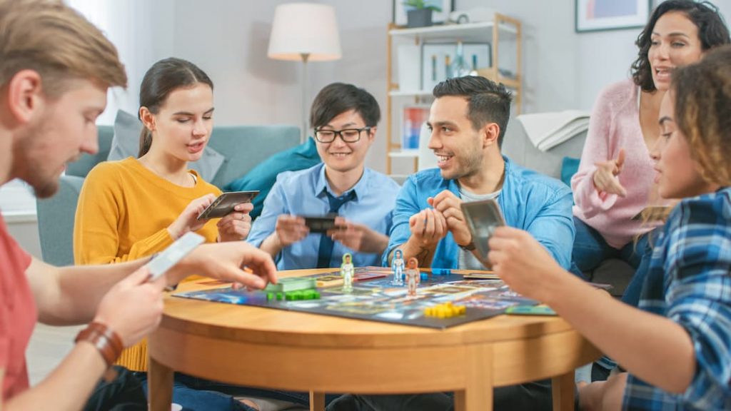 Friends playing a board game around a table | Featured image for top 10 gateway board games blog.