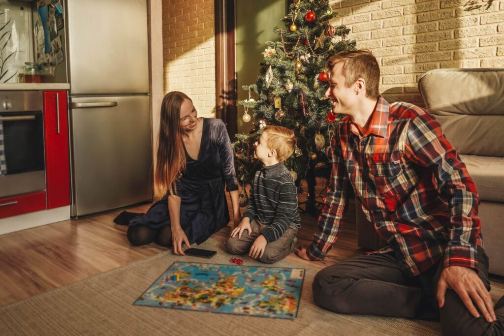 Family playing a board game on Christmas | Featured image for the Best Games for Christmas Parties blog on More Than Meeples.