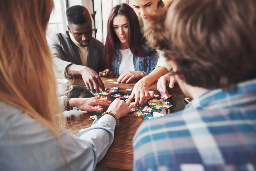 A group of six people sit around a wooden table playing a colorful board game.