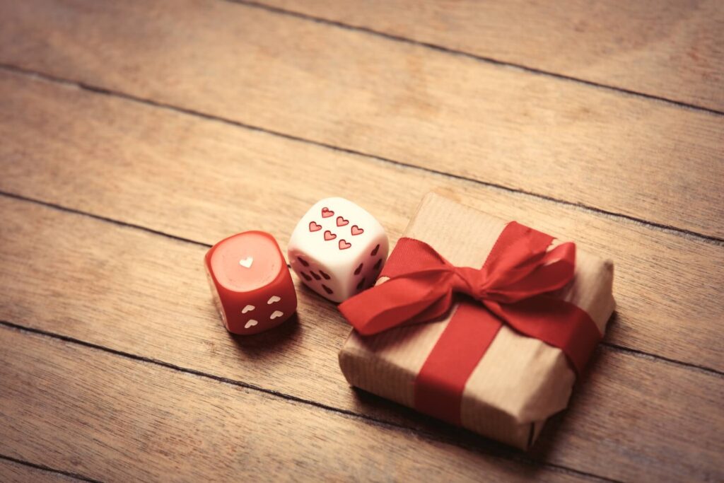 Red and white dice next to a gift wrapped packeage | Featured image for the Board Games That Make Great Gifts blog.