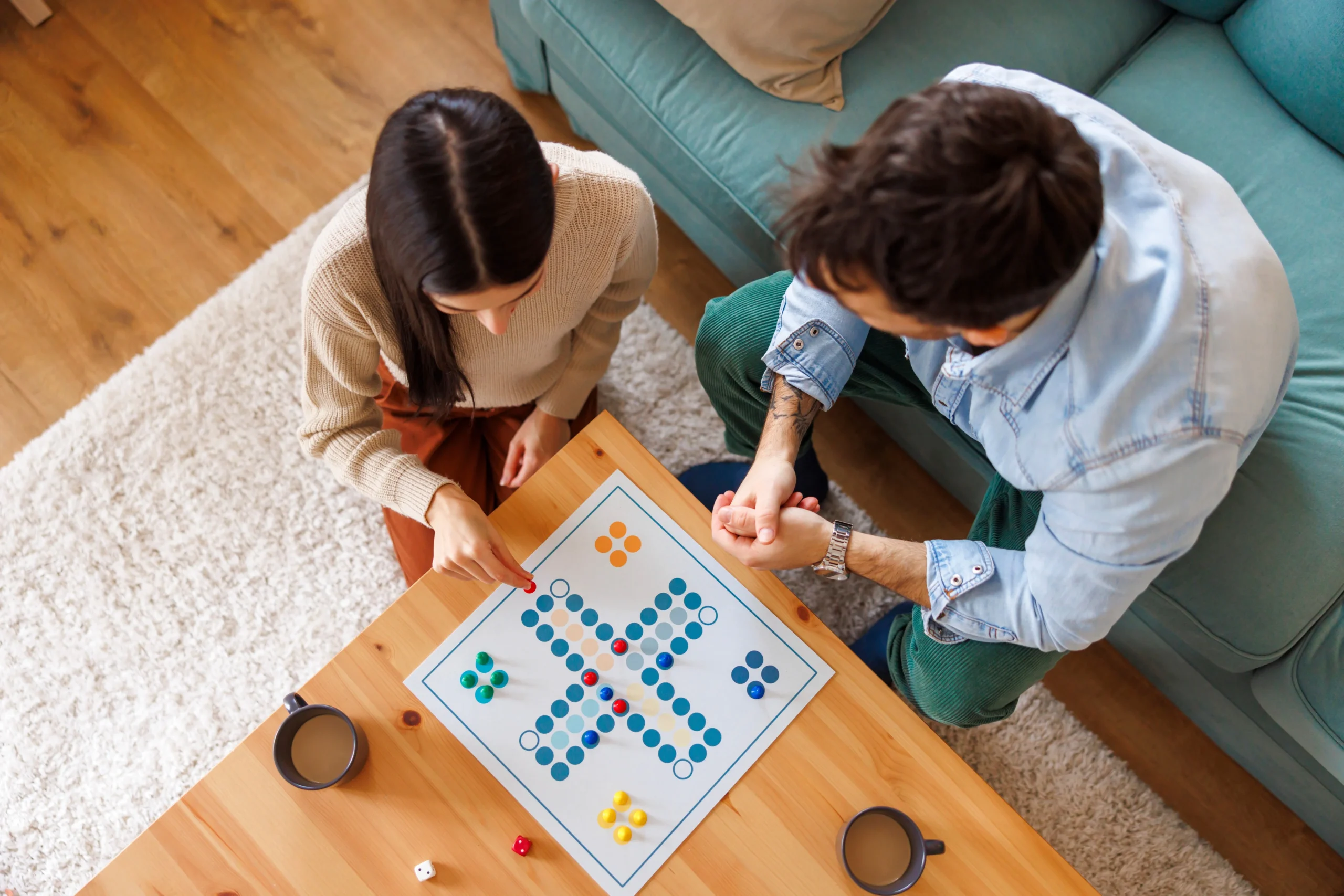 A woman with long, dark hair and a man with dark hair play a board game together on a wooden table.