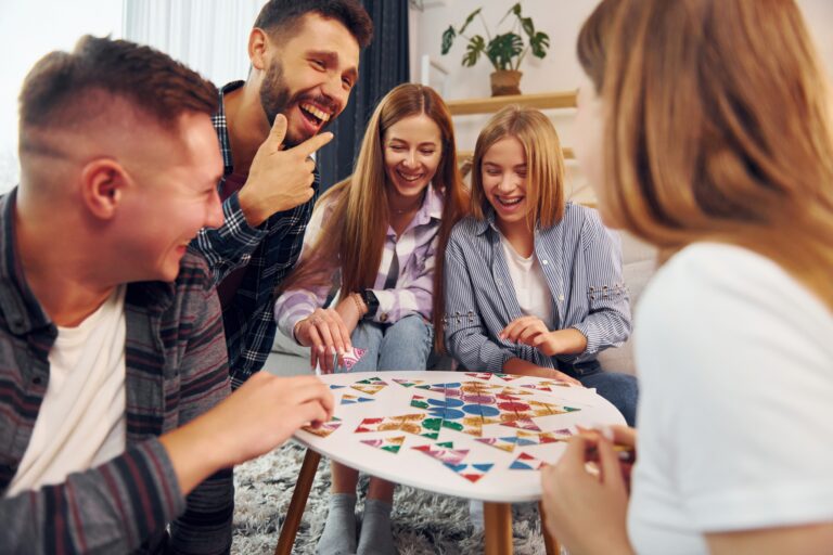 Smiling group of friends crowded around a table with a board game on it